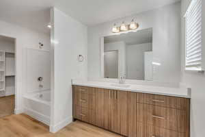 Bathroom featuring vanity, tub / shower combination, light wood-style floors, and a walk in closet