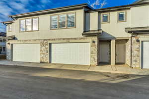 View of front of house with stone siding, stucco siding, and a garage