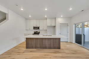 Kitchen with an island with sink, appliances with stainless steel finishes, light wood-style flooring, recessed lighting, and white cabinets