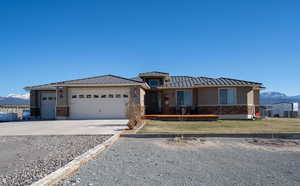 Prairie-style house with a mountain view, stone siding, a standing seam roof, driveway, and an attached garage