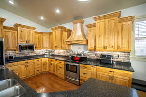 Kitchen with appliances with stainless steel finishes, custom range hood, lofted ceiling, dark wood-style floors, and tasteful backsplash