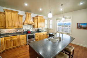Kitchen with stainless steel range with electric stovetop, custom exhaust hood, dark wood finished floors, a center island with sink, and recessed lighting