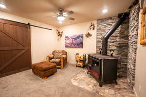 Living area featuring a wood stove, light carpet, a ceiling fan, and a barn door