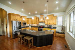 Kitchen featuring pendant lighting, stainless steel appliances, a center island with sink, backsplash, and lofted ceiling