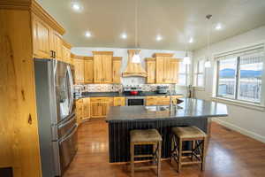 Kitchen featuring stainless steel appliances, pendant lighting, a kitchen island with sink, decorative backsplash, and dark wood finished floors