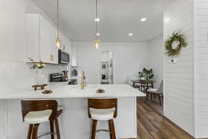 Kitchen with a breakfast bar, a peninsula, appliances with stainless steel finishes, light stone counters, and white cabinets