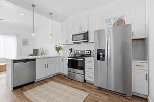 Kitchen with stainless steel appliances, a peninsula, white cabinetry, and decorative light fixtures