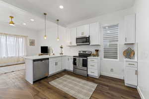 Kitchen featuring white cabinets, appliances with stainless steel finishes, pendant lighting, a peninsula, and dark wood finished floors
