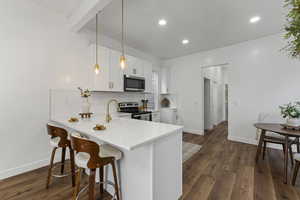 Kitchen featuring a peninsula, stainless steel appliances, a kitchen breakfast bar, dark wood-style floors, and white cabinetry