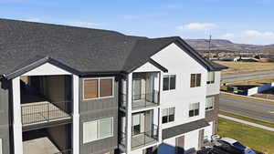 View of front facade with a balcony, a shingled roof, a mountain view, and board and batten siding