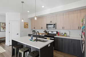 Kitchen featuring light brown cabinetry, a breakfast bar area, an island with sink, pendant lighting, and appliances with stainless steel finishes