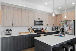 Kitchen featuring light brown cabinetry, modern cabinets, stainless steel appliances, a kitchen breakfast bar, and hanging light fixtures