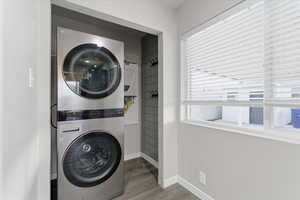 Washroom with stacked washer and clothes dryer and wood finished floors