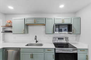Kitchen featuring stainless steel appliances, backsplash, open shelves, light stone countertops, and green cabinetry