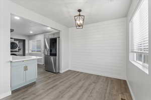 Unfurnished dining area featuring estacked washer and dryer, light wood-style flooring, a chandelier, wood walls, and recessed lighting