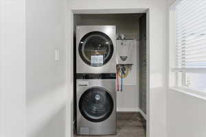 Laundry room with stacked washer / dryer, water heater, and concrete floors