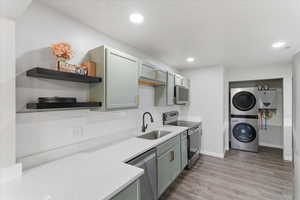Kitchen featuring stainless steel appliances, light wood-style flooring, open shelves, stacked washer and clothes dryer, and light stone counters