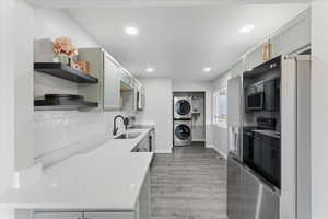 Kitchen featuring stacked washer and clothes dryer, open shelves, tasteful backsplash, light wood-type flooring, and appliances with stainless steel finishes