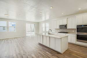 Kitchen featuring tasteful backsplash, appliances with stainless steel finishes, light wood-style flooring, a center island with sink, and a textured ceiling