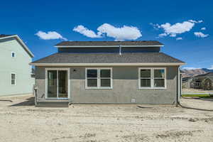 Back of property featuring a shingled roof and stucco siding