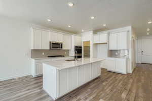 Kitchen with tasteful backsplash, white cabinetry, light wood-style flooring, stainless steel appliances, and a textured ceiling