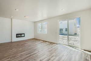 Unfurnished living room featuring a glass covered fireplace, light wood-type flooring, and a textured ceiling