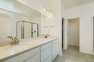 Bathroom with a shower stall, double vanity, and light tile patterned floors