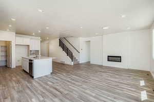 Kitchen featuring a glass covered fireplace, open floor plan, a center island with sink, white cabinetry, and light wood finished floors