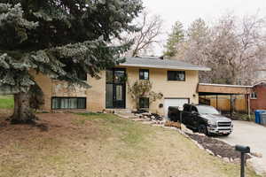 Split foyer home with concrete driveway, a carport, brick siding, a garage, and a front lawn