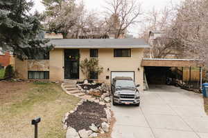 View of front of property with driveway, a chimney, brick siding, an attached carport, and a garage