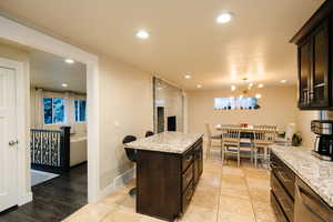 Kitchen featuring a breakfast bar, recessed lighting, light stone counters, dark brown cabinetry, and dishwasher