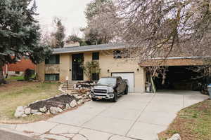 Split foyer home featuring brick siding, an attached garage, a chimney, driveway, and a front yard