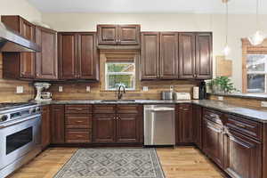 Kitchen with stainless steel appliances, dark brown cabinets, dark stone countertops, and wall chimney range hood