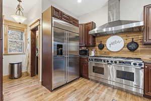 Kitchen with wall chimney range hood, high end appliances, dark brown cabinetry, and hanging light fixtures