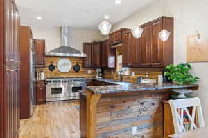 Kitchen with premium appliances, pendant lighting, wall chimney exhaust hood, a peninsula, and backsplash