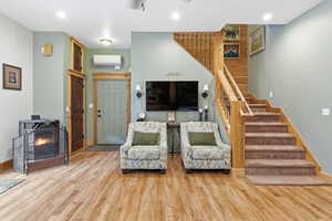 Living room with a wood stove, stairs, light wood-style flooring, recessed lighting, and a wall unit AC