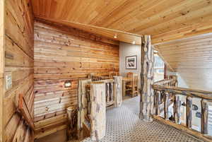 Hallway with an upstairs landing, wood walls, wooden ceiling, and vaulted ceiling