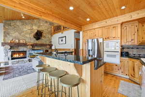 Kitchen with a kitchen breakfast bar, wooden ceiling, a stone fireplace, white appliances, and a kitchen island