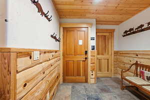 Entrance foyer featuring wood ceiling, a wainscoted wall, stone tile flooring, and wooden walls