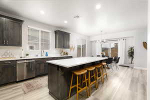 Kitchen featuring a breakfast bar, dishwasher, dark brown cabinetry, recessed lighting, and light wood-style flooring