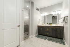 Primary bathroom featuring double vanity, light tile patterned floors, a shower stall, and a ceiling fan