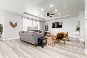 Living room featuring a raised ceiling, recessed lighting, a ceiling fan, and light wood-type flooring