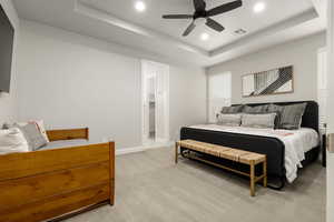 Primary bedroom featuring a tray ceiling, light colored carpet, recessed lighting, and a ceiling fan