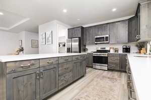 Kitchen featuring appliances with stainless steel finishes, recessed lighting, light wood-style flooring, dark brown cabinetry, and light stone countertops