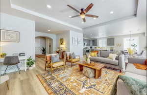 Living area featuring wood finished floors, arched walkways, ceiling fan, recessed lighting, and a tray ceiling