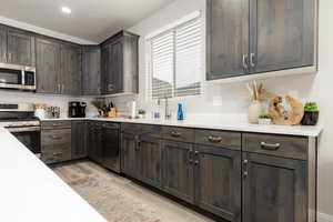 Kitchen featuring dark brown cabinets, appliances with stainless steel finishes, light wood-style flooring, light stone countertops, and recessed lighting