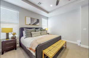 Primary bedroom featuring light colored carpet, a ceiling fan, recessed lighting, and a tray ceiling