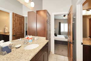 Ensuite bathroom featuring vanity, light colored carpet, light tile patterned flooring, and a ceiling fan