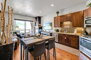 Kitchen with stainless steel appliances, light stone counters, light wood finished floors, backsplash, and recessed lighting