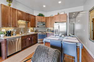 Kitchen with backsplash, appliances with stainless steel finishes, light stone counters, light wood-style floors, and recessed lighting